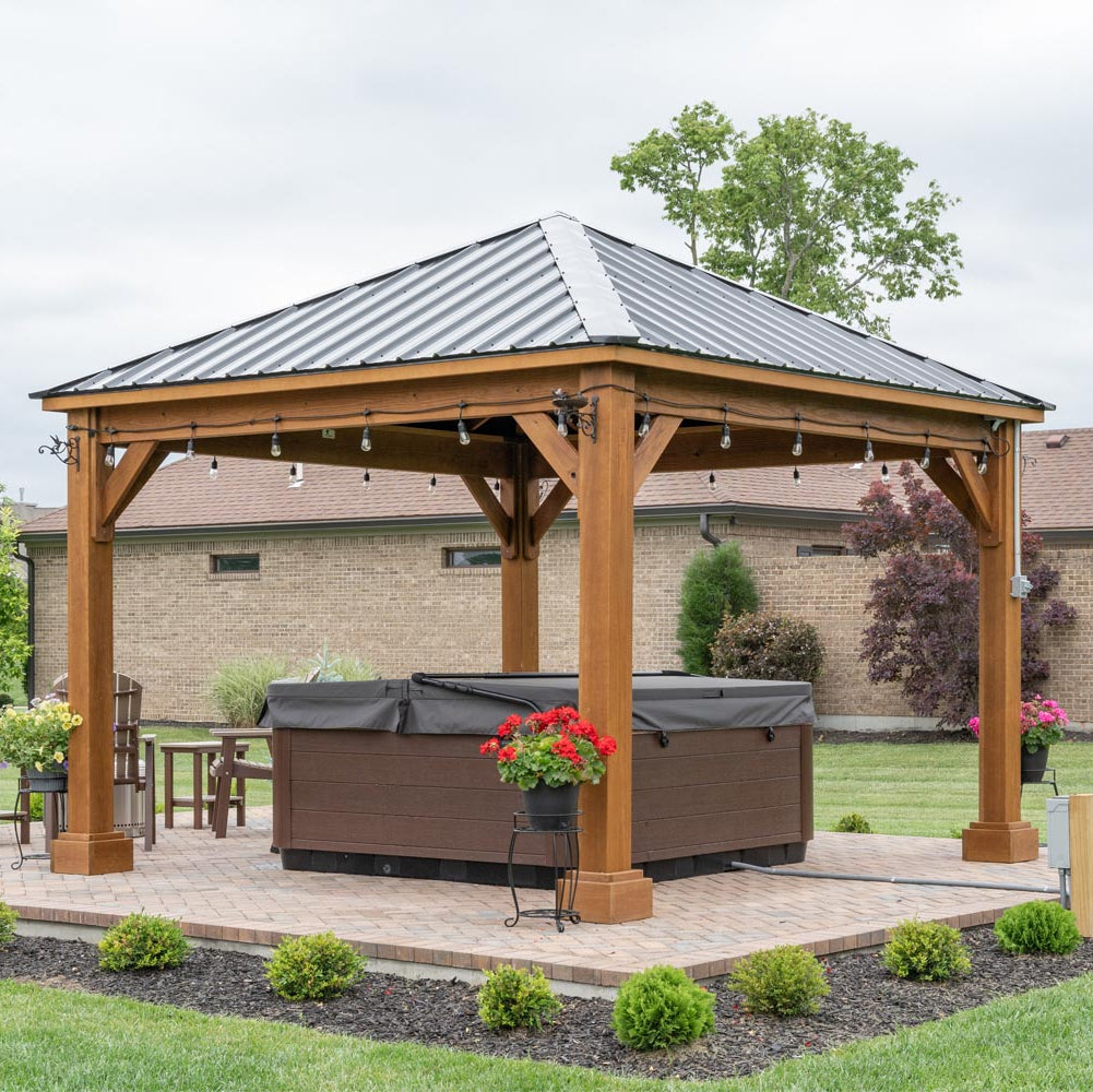 Wooden gazebo with a hot tub underneath, surrounded by a garden setting.